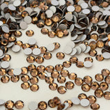 Preciosa crystal smoked topaz colour faceted round rhinestones with silver dura foiling scattered on a white surface