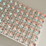 A group of Swarosvki article 3200 Rivoli sew on stones in white packaging tray showing 2 hole design and Crystal Shimmer colour