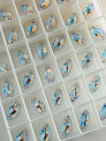 A group of Swarovski article 3223  navette-shaped faceted rhinestones Crystal Shimmer colour, arranged in a white plastic organizer.