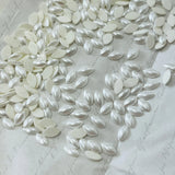 White pearl-effect navette hotfix crystals, oval cabochons scattered on flat surface