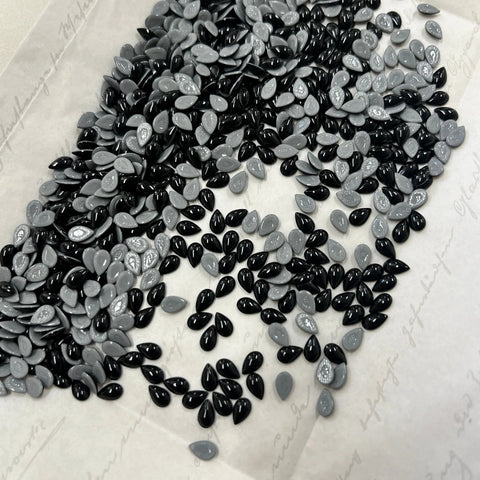 Jet black and silver pear-shaped hotfix cabochon crystals, drop style on white backing.