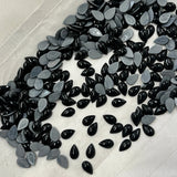 Black and silver drop pear hotfix cabochon crystals scattered on white backing.