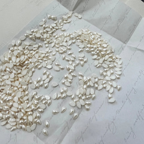 Pear-shaped pearl-effect hotfix crystals, cream/white, scattered on backing sheet